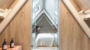 A bedroom with a sloped ceiling, a bed with a white cover, and two bottles of shampoo on a marble surface. - Luxury & Design duplex - 5 min from Louvre Museum - 6 guests (Paris)
