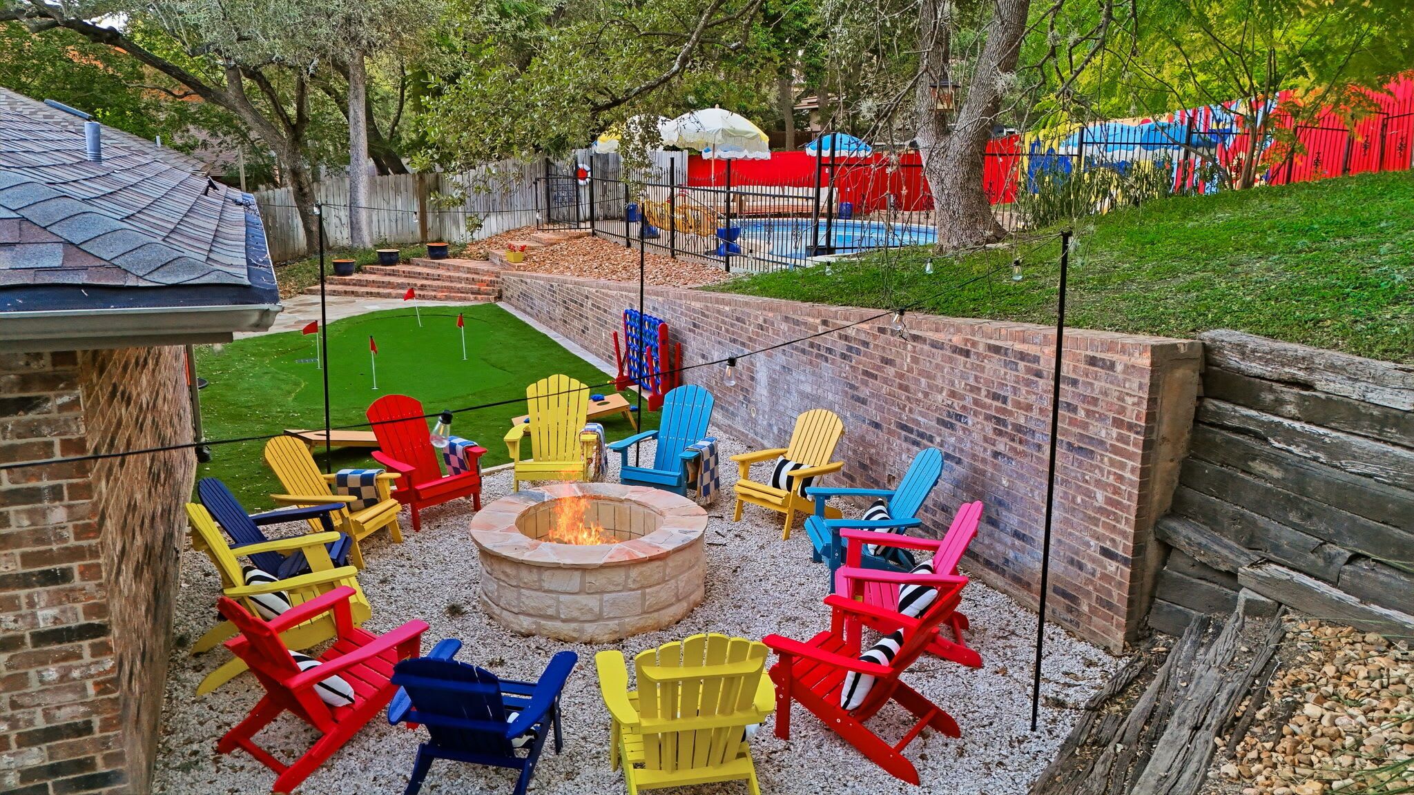 A backyard with a fire pit, colorful Adirondack chairs, and a small pool area.