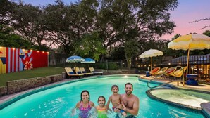 Una piscina con sillas de descanso y sombrillas, rodeada por una valla y árboles.