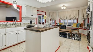 Una cocina moderna con armarios blancos, una isla central y una zona de comedor con un banco y cojines.