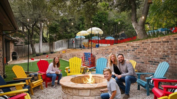 Un patio trasero con un brasero, sillas Adirondack de colores y un muro de ladrillo.