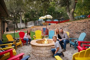 A backyard with a fire pit, colorful Adirondack chairs, and a brick wall. - Sleeps 16! Heated Pool, Hot Tub, & Sport Court (San Antonio)