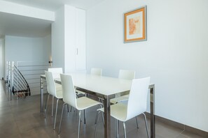 Un comedor moderno con una mesa y sillas blancas, una escalera y un cuadro en la pared.