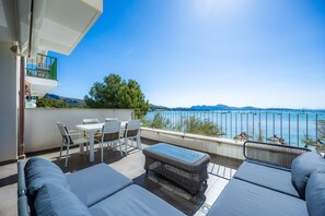 A balcony with a table and chairs, a sofa, and a view of the sea.
