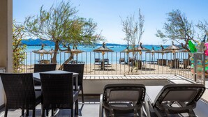 A terrace with wicker furniture, umbrellas, and a view of the beach and sea. - Apartment 'Voramar 33A Joana Duplex' with Sea View, Private Terrace and Wi-Fi (Port Pollensa)