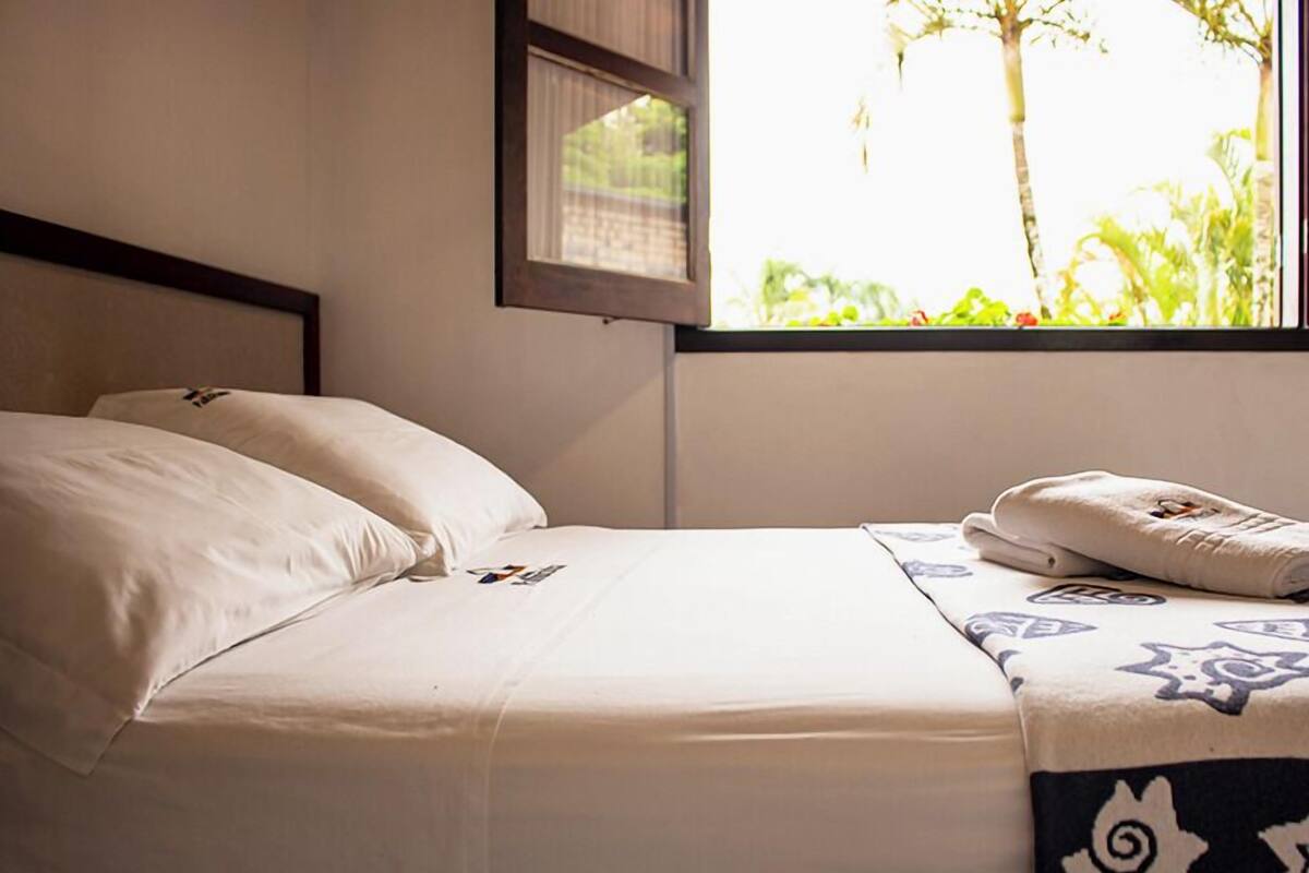 A bed with a white mattress and pillows, a patterned blanket, and a towel on the side.