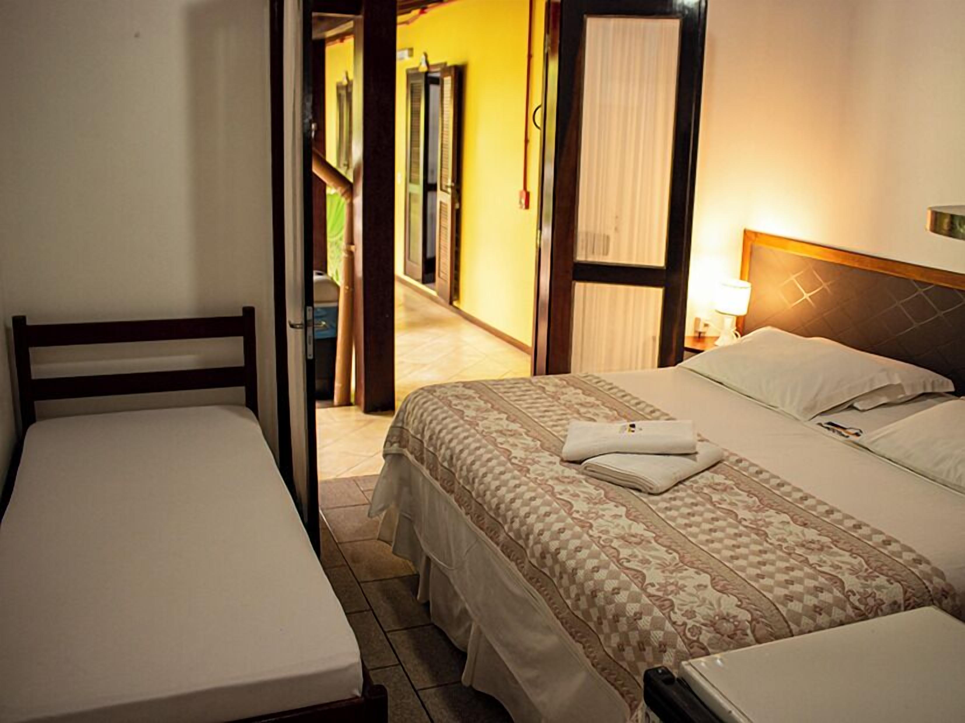 Une chambre d’hôtel avec deux lits simples, une tête de lit en bois, une table de chevet avec une lampe et une vue sur l’espace extérieur.