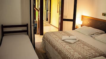 Une chambre d’hôtel avec deux lits simples, une tête de lit en bois, une table de chevet avec une lampe et une vue sur l’espace extérieur.