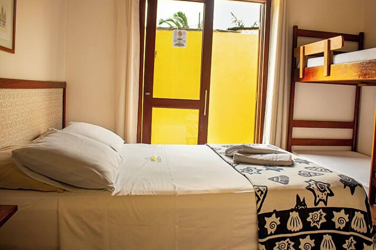 A hotel room with a bed, a window with a view of a yellow building, and a bunk bed.