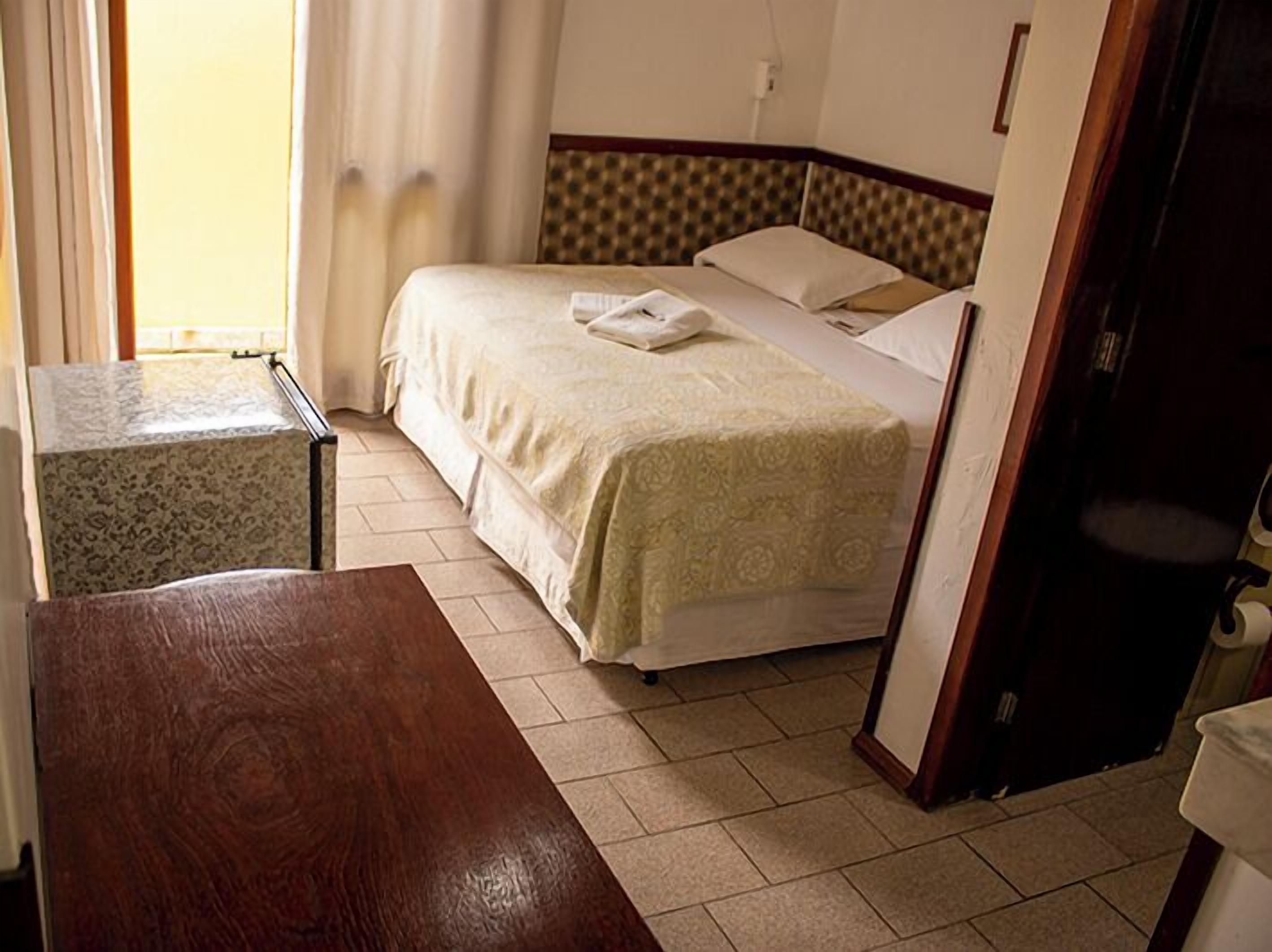 A hotel room with a bed, a small table, and a wooden bench.