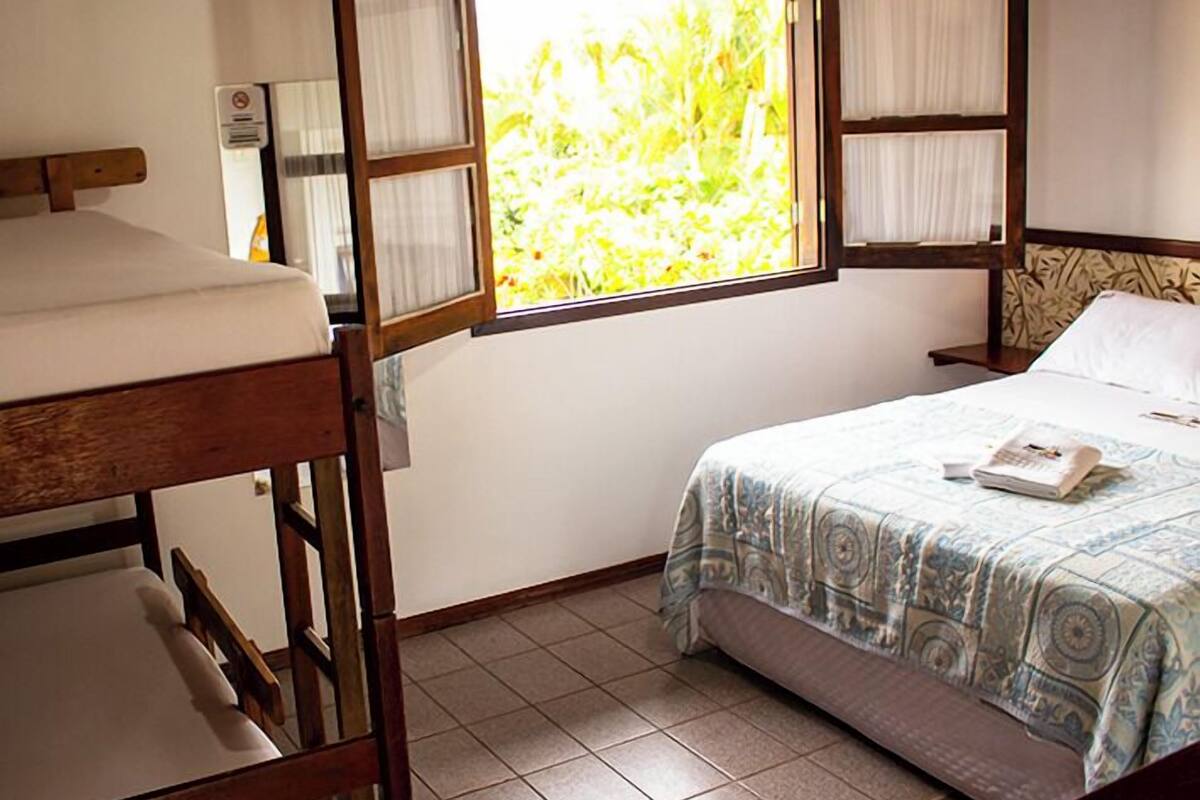 A room with a bed, a wooden bunk bed, and a window with curtains.