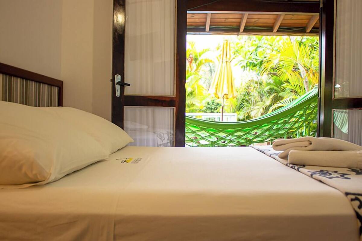 A bed with a white sheet and a pillow, a green hammock, and a towel on a table.