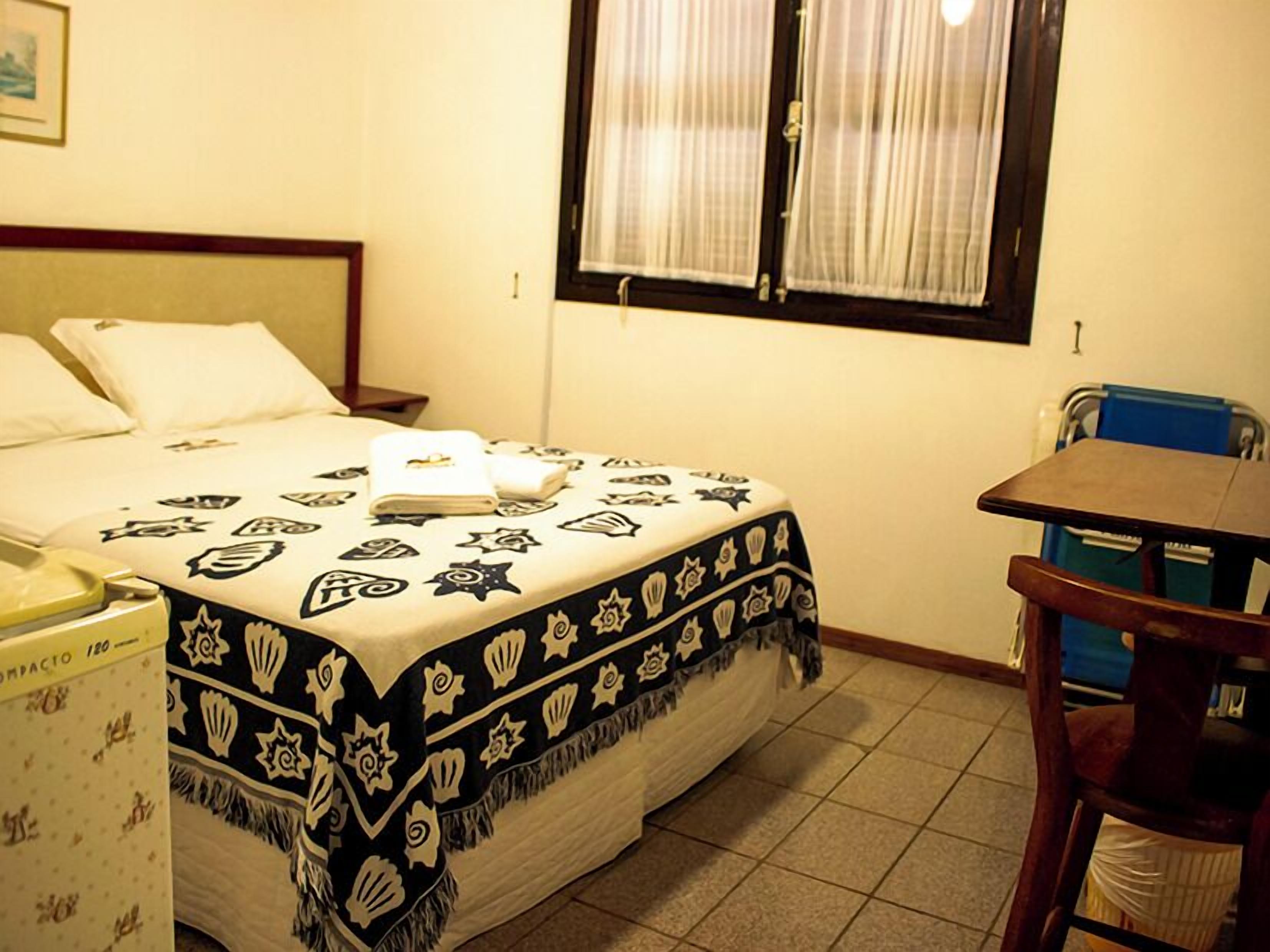 Une chambre d’hôtel avec un lit, une table de chevet, une chaise, une fenêtre avec des rideaux et une petite table.