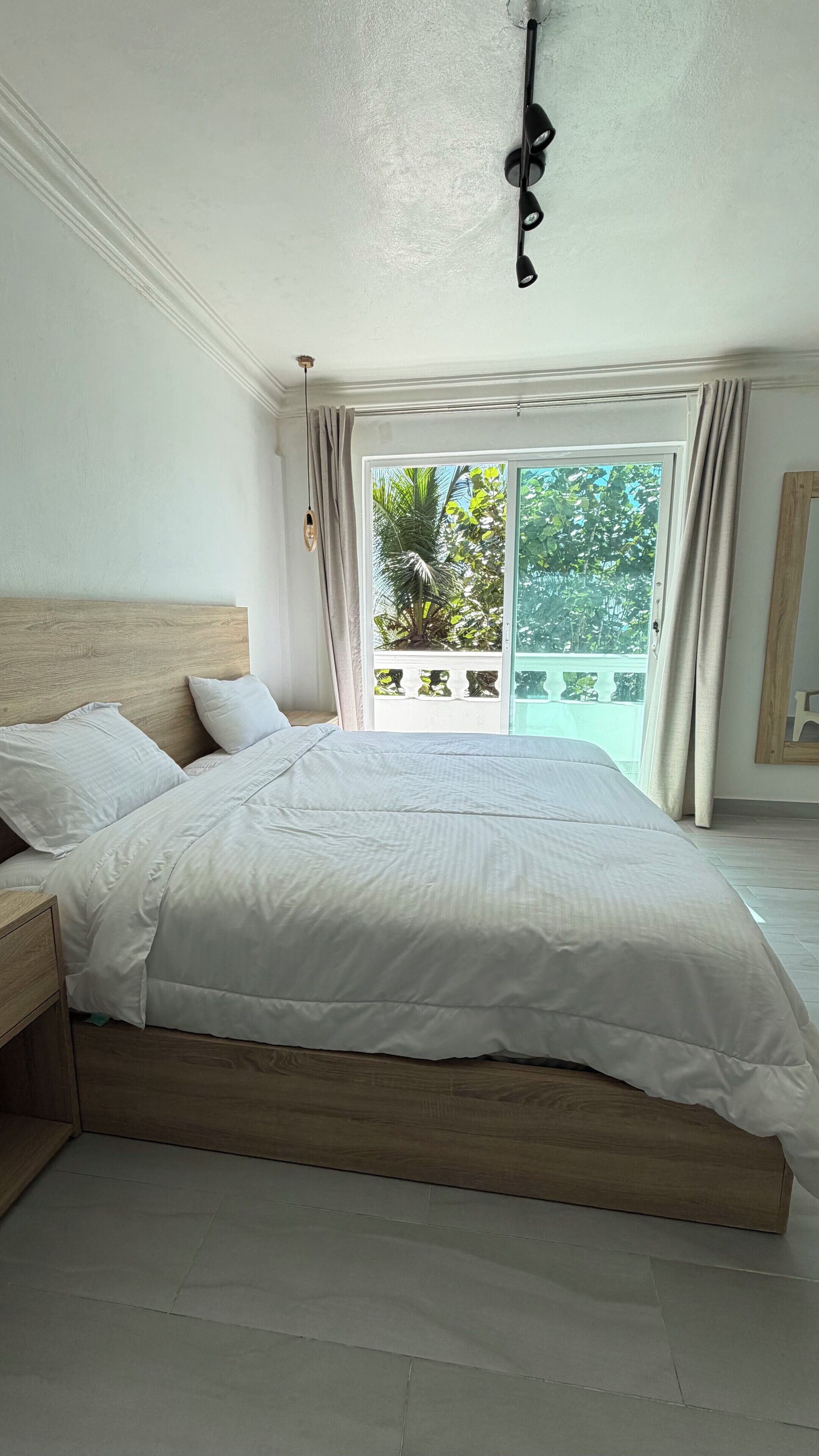 A bedroom with a large bed, wooden headboard, and a view of greenery through a sliding glass door.