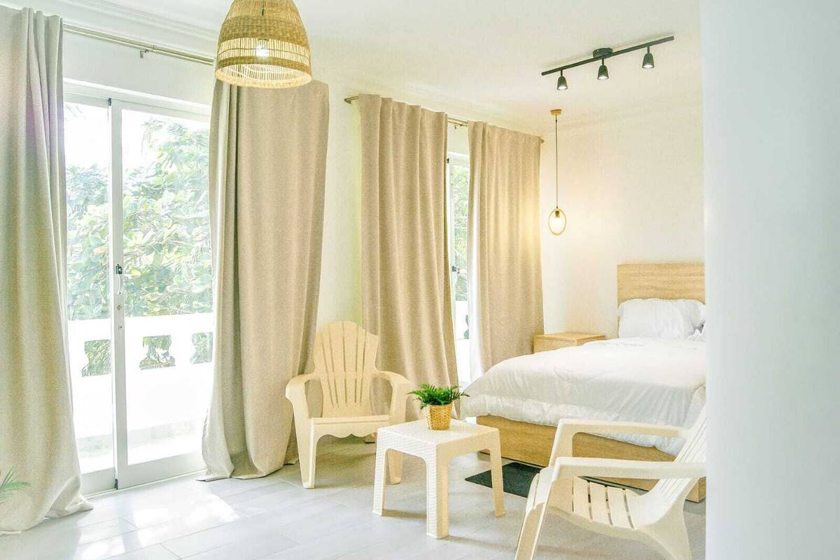A bedroom with a bed, a chair, a small table, and a hanging light fixture.