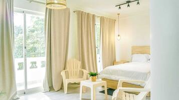 A bedroom with a bed, a chair, a small table, and a hanging light fixture.