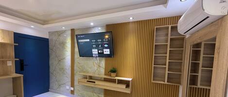 A modern bedroom with a bed, a TV mounted on the wall, a wooden shelf, and a built-in wardrobe.