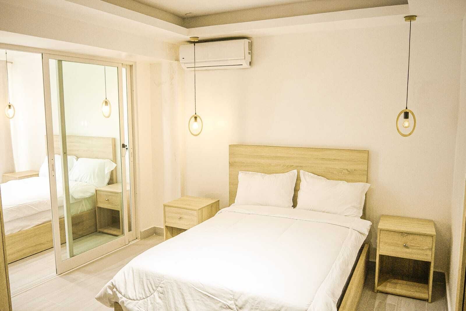 Un dormitorio con una cama grande, dos mesitas de noche, un ventanal corredero y un equipo de aire acondicionado.