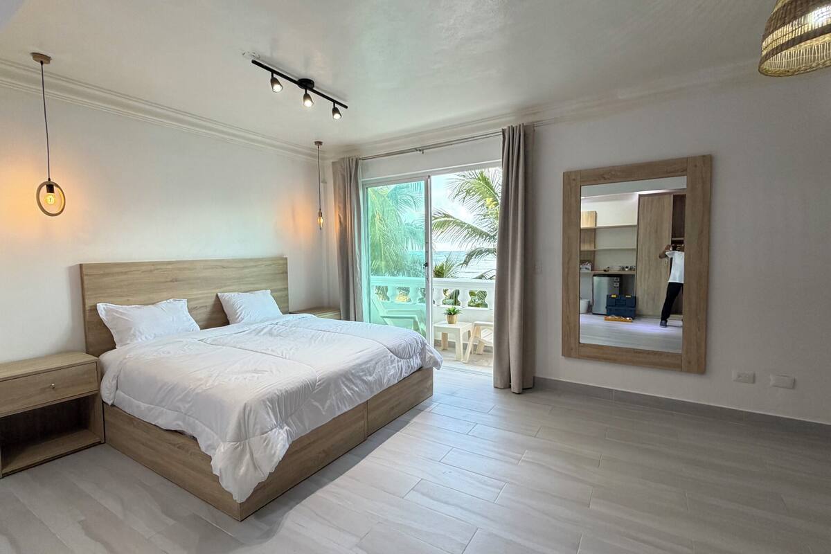 A bedroom with a wooden bed, a nightstand, a mirror, and a view of the outdoors.