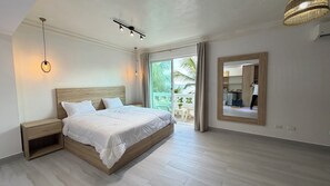 A bedroom with a wooden bed, a nightstand, a mirror, and a view of the outdoors. - Hotel Juan Dolio (Guayacanes)