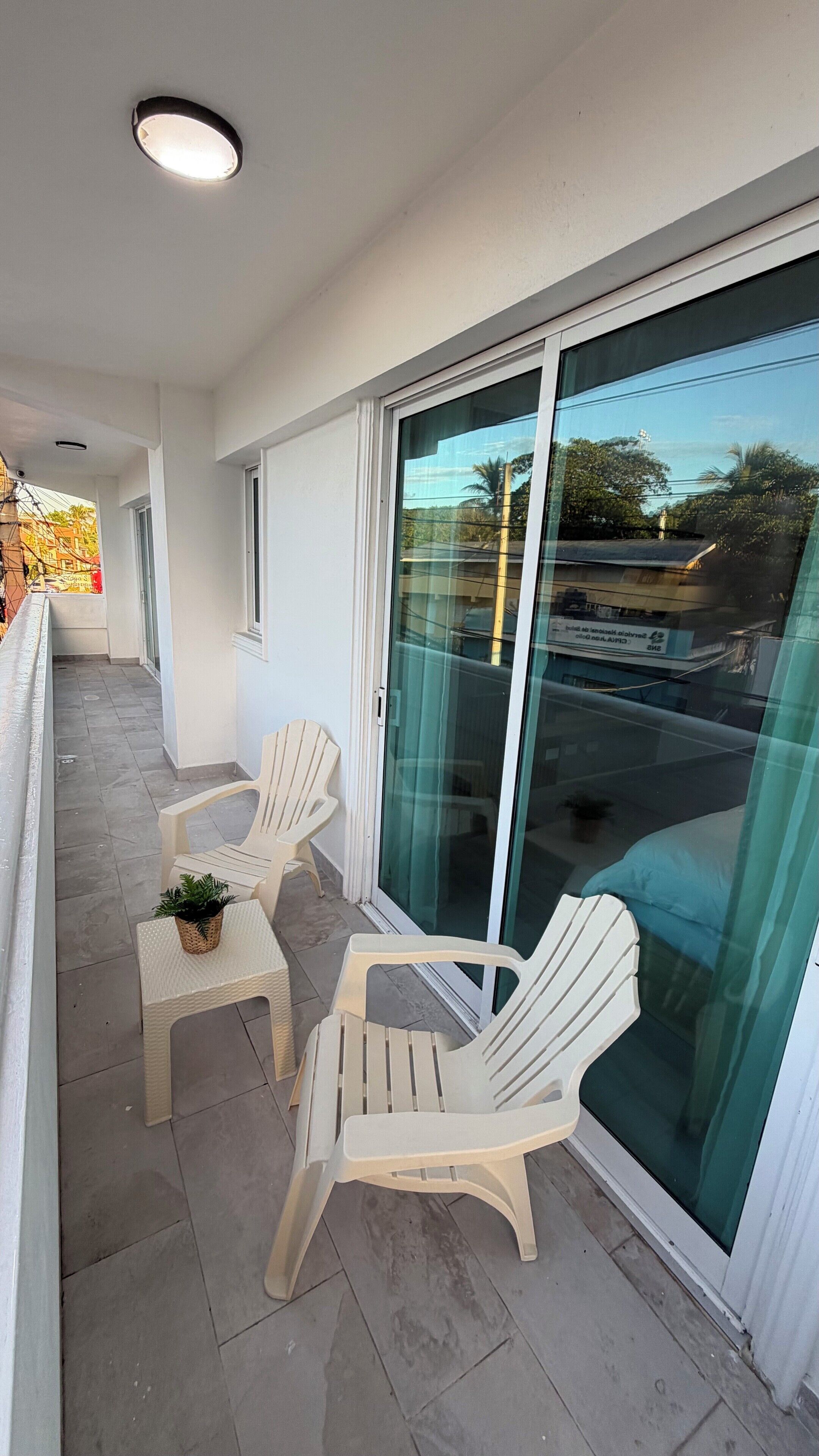 A balcony with two white plastic chairs and a small table, a glass door, and a view of a parking area.