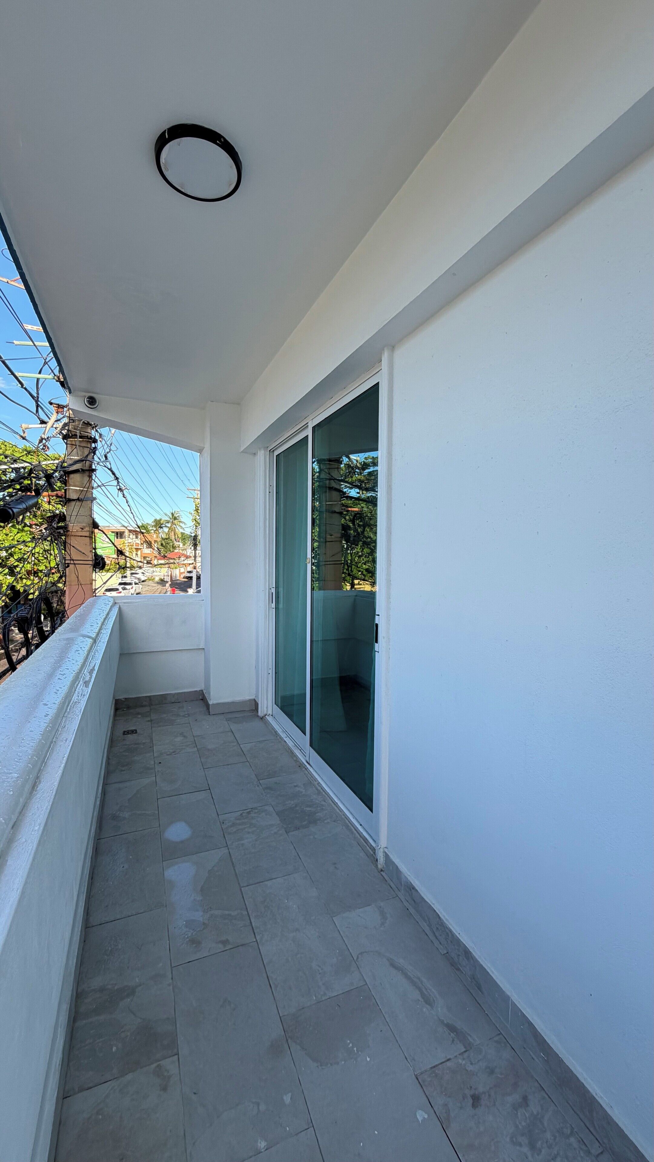 A balcony with a tiled floor, a glass door, and a view of a street with buildings and cars.
