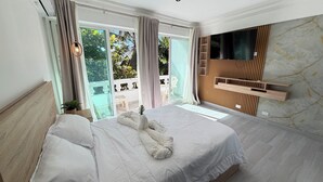 Une chambre d’hôtel moderne dotée d’un grand lit, d’un téléviseur fixé au mur et d’un balcon offrant une vue sur la verdure.