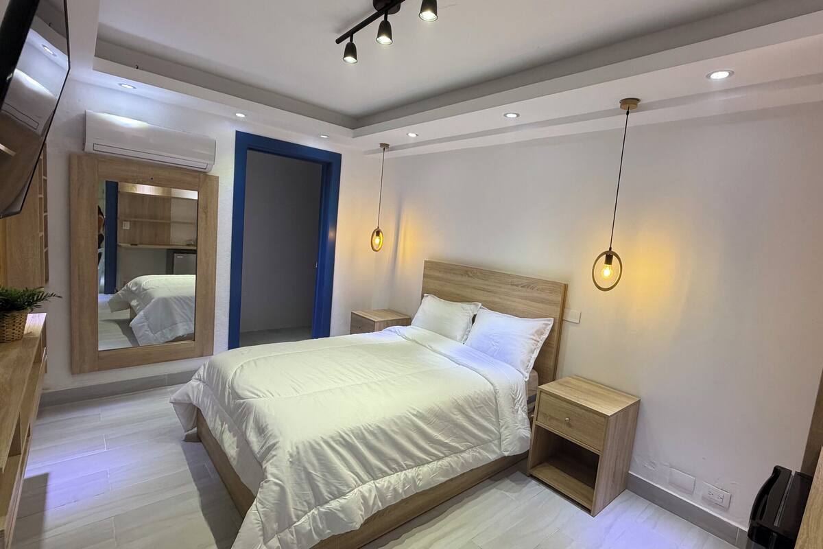 A modern bedroom with a large bed, bedside tables, a mirror, and a TV.