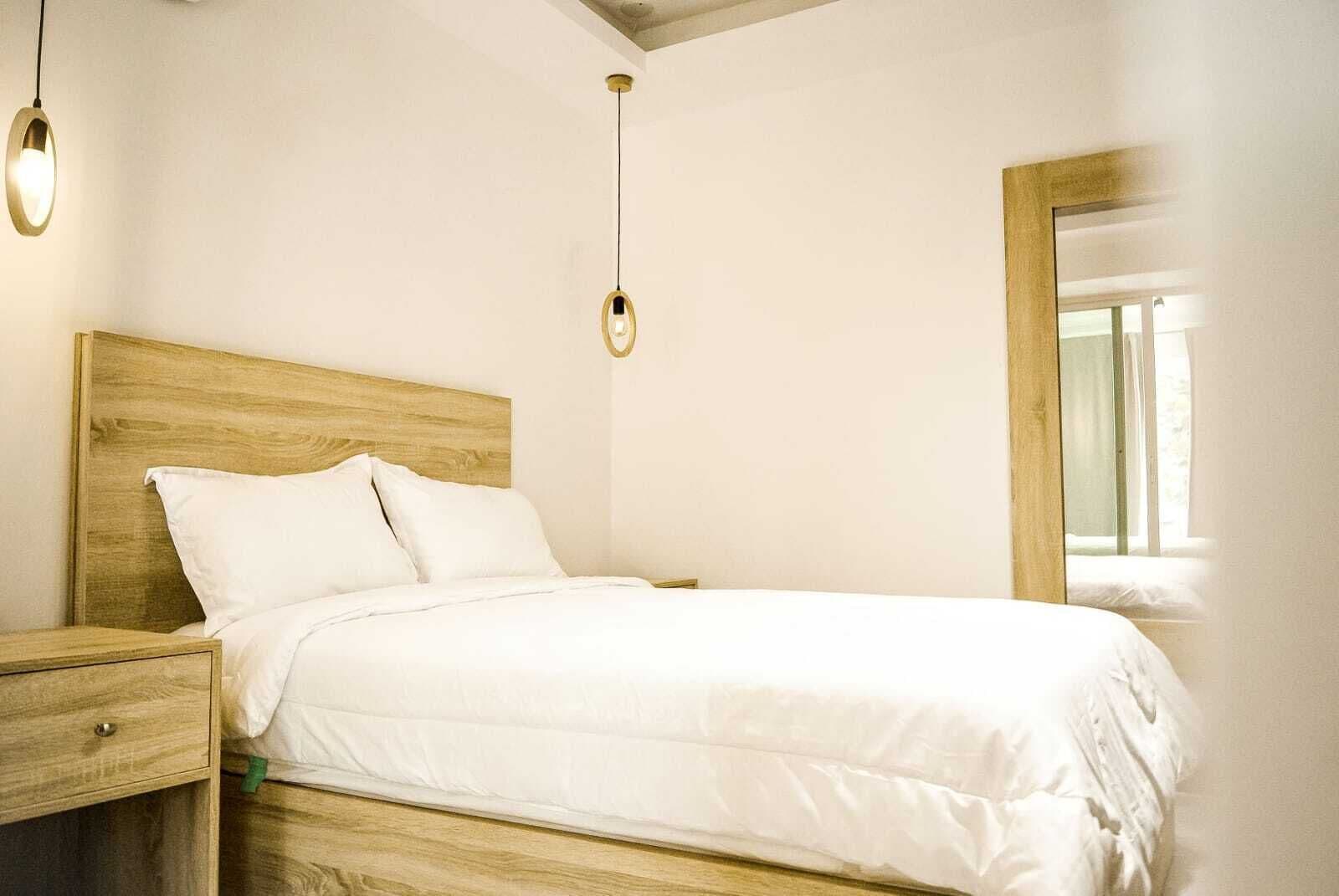 Un letto rifatto con cura, una testiera in legno, un comodino con un cassetto e due lampade a sospensione.