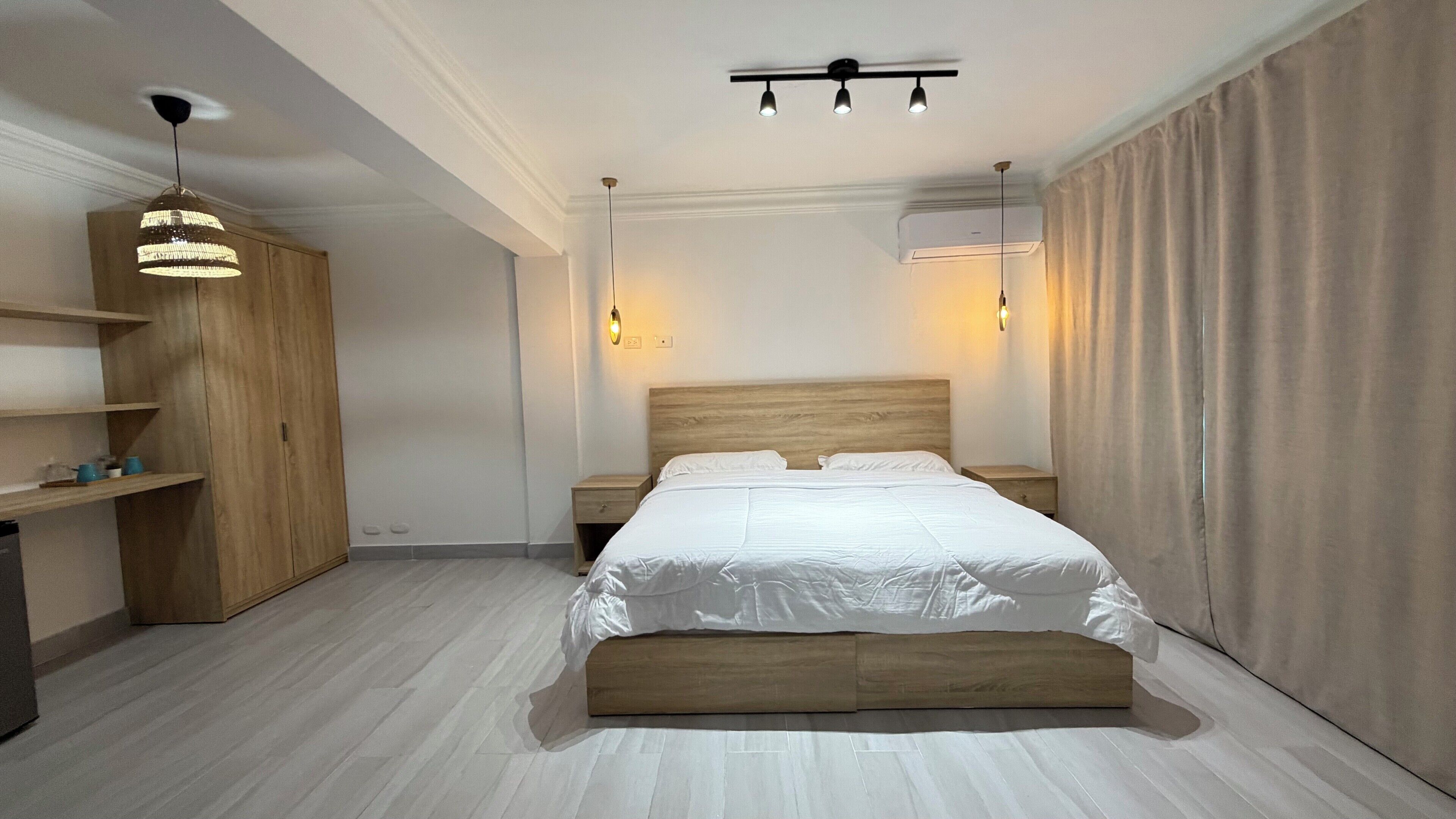 Ein modernes Schlafzimmer mit einem großen Bett, einem Holz-Kopfteil, Nachttischen, einem Kleiderschrank und Pendelleuchten.