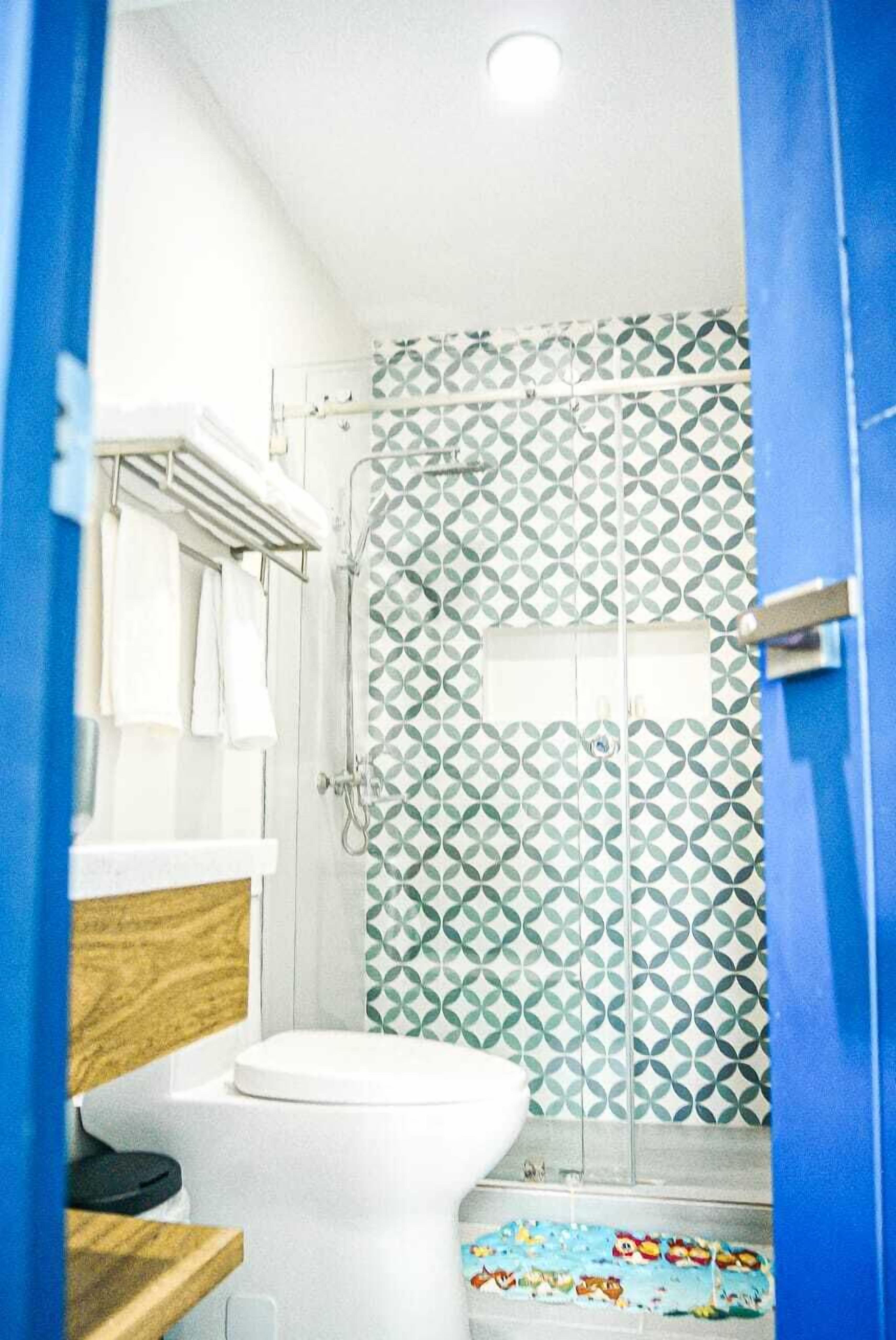 A bathroom with a white toilet, a wooden vanity, a shower with a geometric tile pattern, and a blue door.