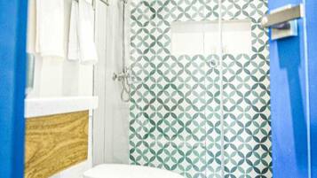 A bathroom with a white toilet, a wooden vanity, a shower with a geometric tile pattern, and a blue door.