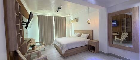 Una habitación de hotel moderna con una cama grande, un escritorio con silla, televisor y un espejo amplio.