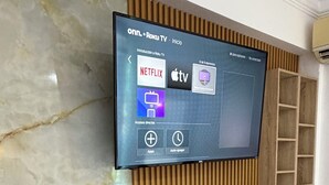 Un téléviseur à écran plat fixé au mur, avec un panneau décoratif en bois et une surface en dessous qui ressemble à du marbre.