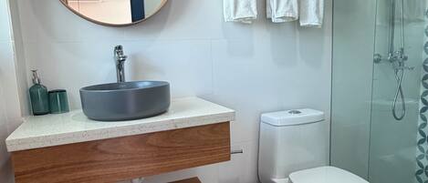 Een moderne badkamer met een ronde spiegel, een wastafel op een voetstuk, een toilet en een douchecabine van glas.