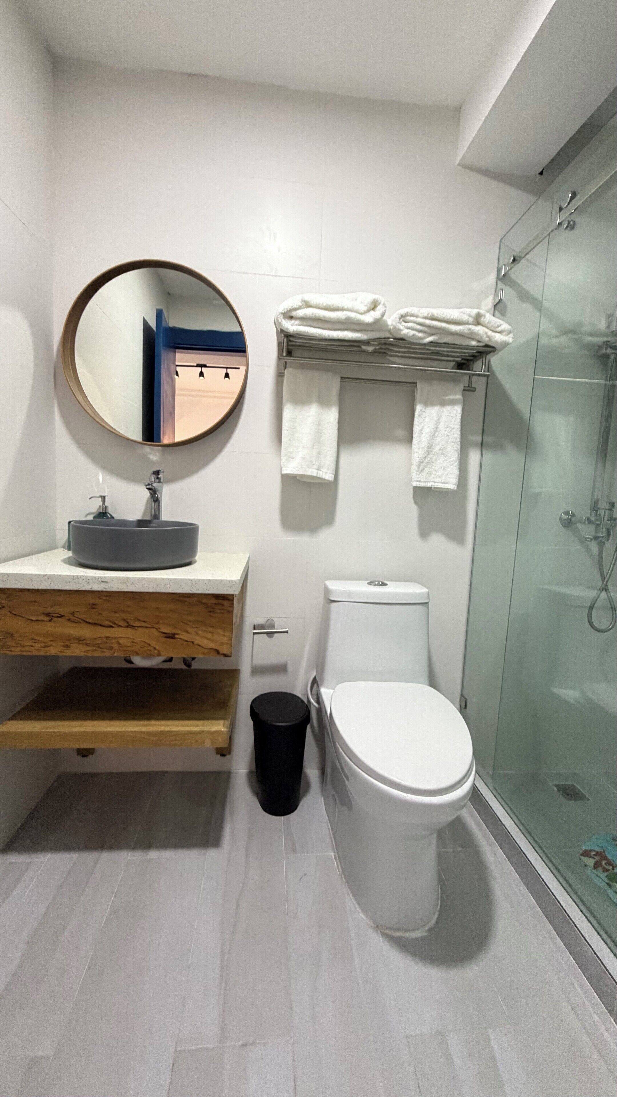 A modern bathroom with a round mirror, a sink, a toilet, and a glass shower enclosure.