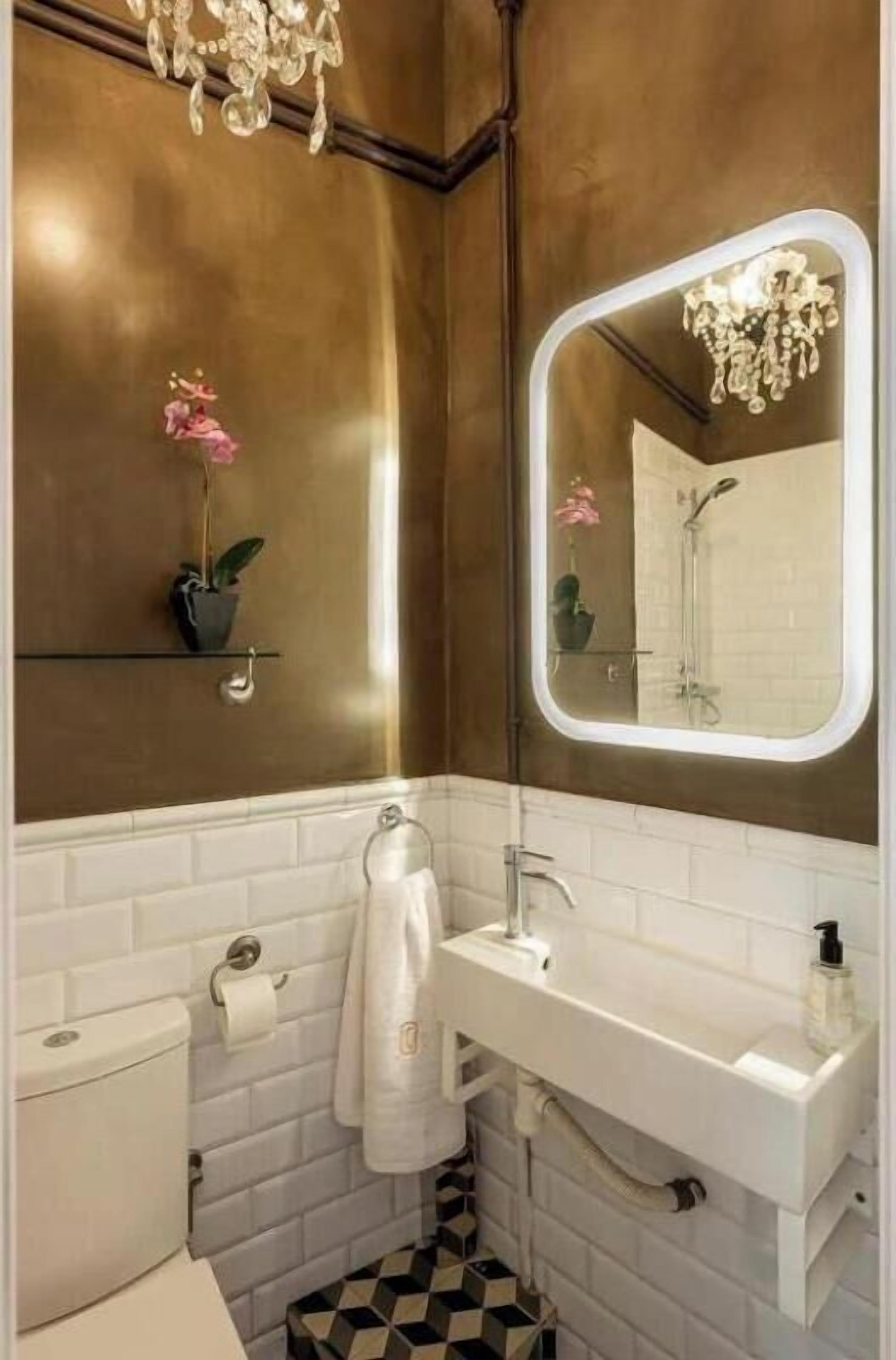Un baño con un lavamanos blanco, un espejo con marco iluminado, un inodoro y un suelo con estampado.