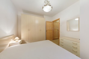 Een slaapkamer met een bed, nachtkastje, dressoir, kledingkast en spiegel.