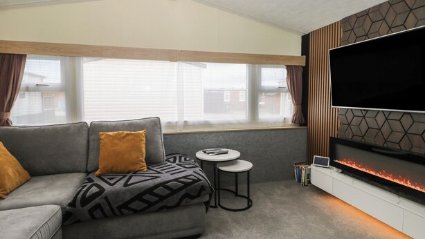Ein modernes Wohnzimmer mit einem grauen Sofa, einem kleinen runden Tisch, einem Flachbildfernseher an einer Wand mit geometrischem Muster und einem Kamin.