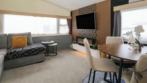 Ein modernes Wohnzimmer mit einer Couch, einem kleinen runden Tisch, einem Kamin und einem an einer Wand mit geometrischem Muster befestigten Fernseher.