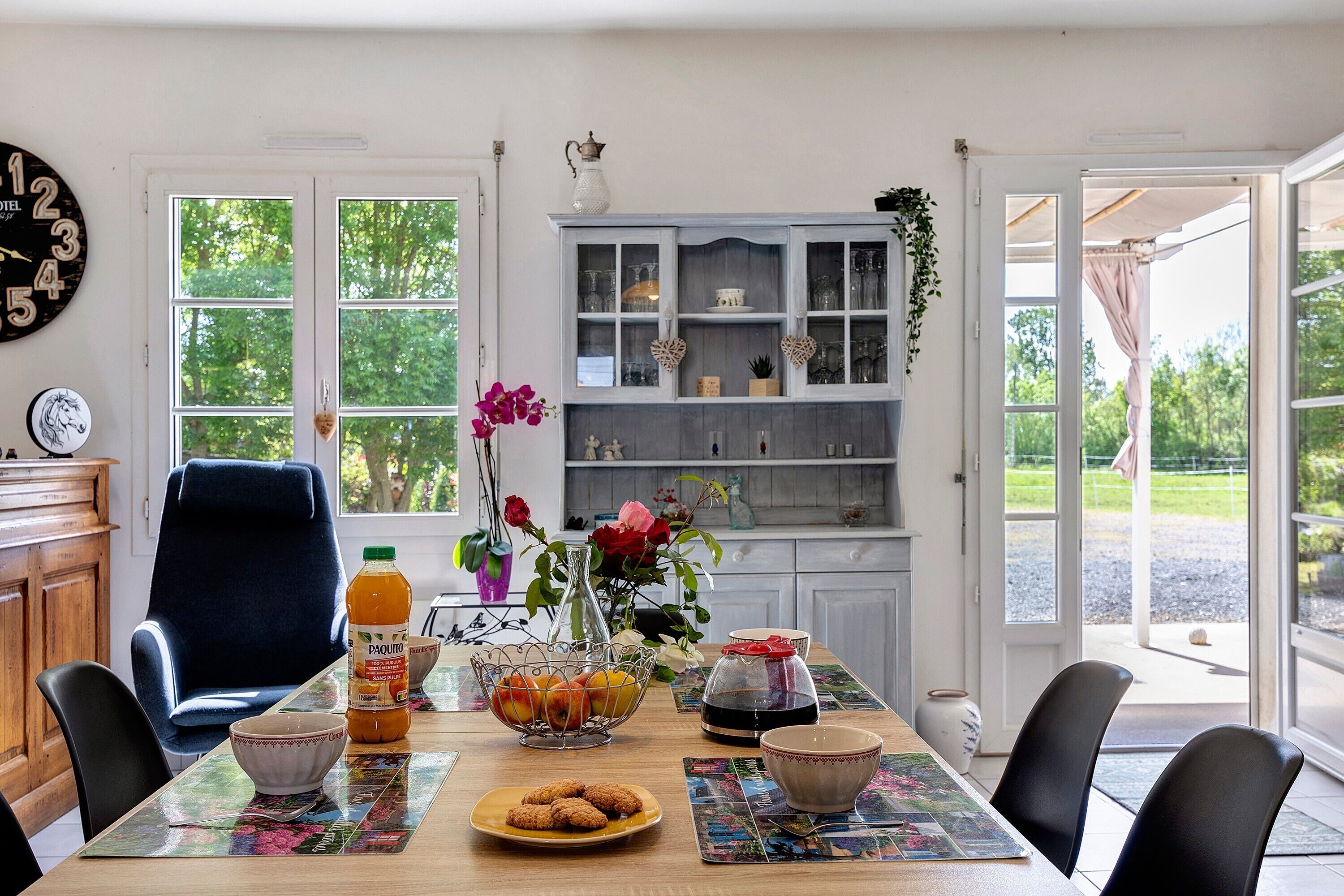 Une table à manger avec un panier de fruits, une bouteille de jus et un vase rempli de fleurs.