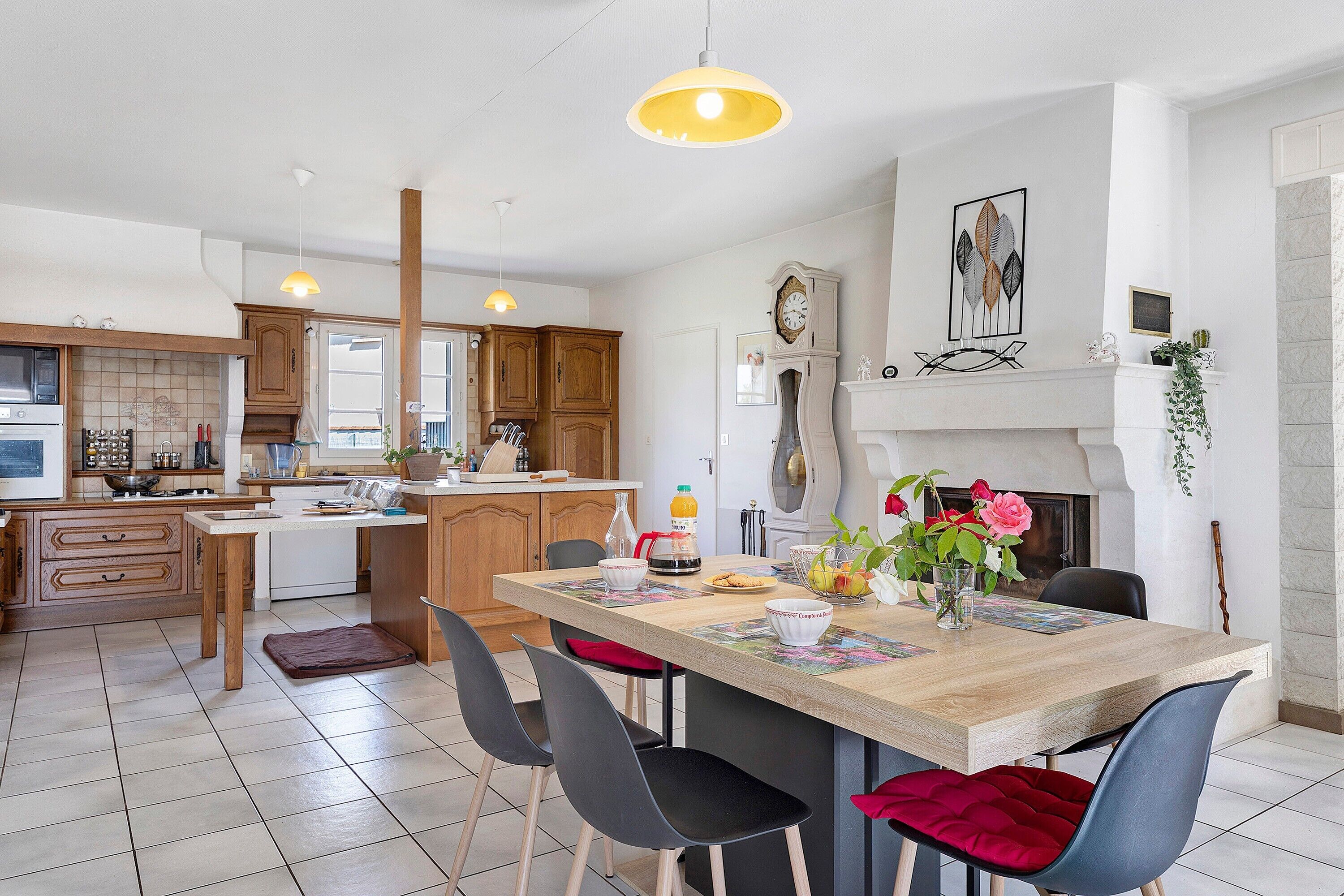 A modern kitchen with wooden cabinets, a central island, and a dining area with chairs and a table.
