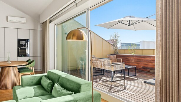 En moderne lejlighed med en grøn sofa, et spiseområde og en balkon med udendørs møbler.