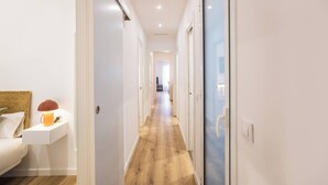 A hallway with a wooden floor, white walls, and a bed with a lamp on a nightstand. - 63IND1125- Brand new apartment (Barcelona)