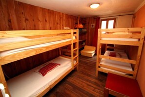 Ett rum med våningssängar i trä, ett litet bord och en hylla med diverse föremål.