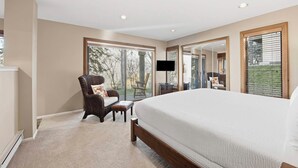 A bedroom with a large bed, a chair, a TV, and a window with a view of trees. - Ridgepoint Townhome 090 (Beaver Creek)