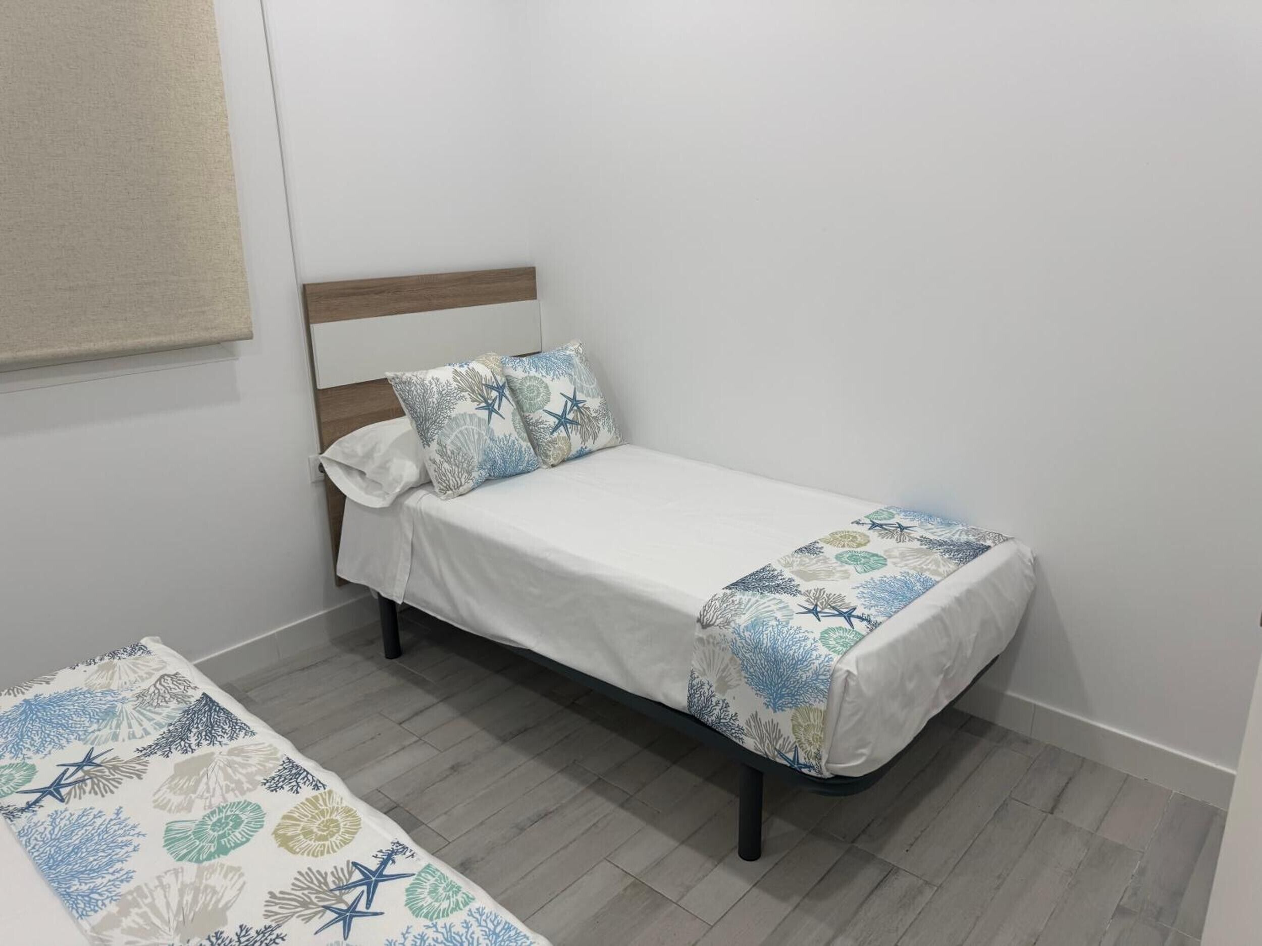 A single bed with a white mattress, two pillows, and a patterned bedspread.