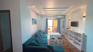 A modern living room with a sofa, a TV, and a dining area with a table and chairs. - Casablanca resort Hurghada Red Sea (Hurghada)