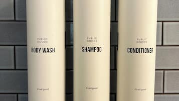Tres recipients de productes de bany etiquetats com 'BODY WASH', 'XAMPO' i 'CONDITIONER' penjats a la paret.