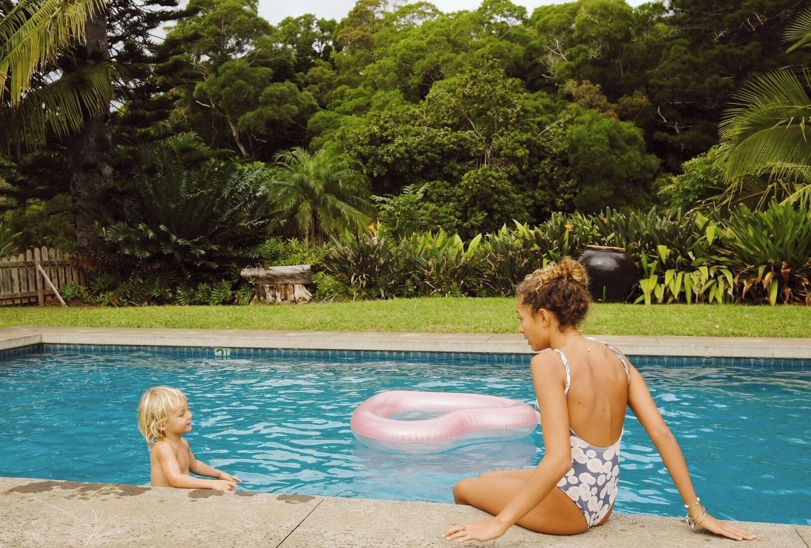 Une piscine avec une terrasse en bois et une végétation luxuriante en arrière-plan.